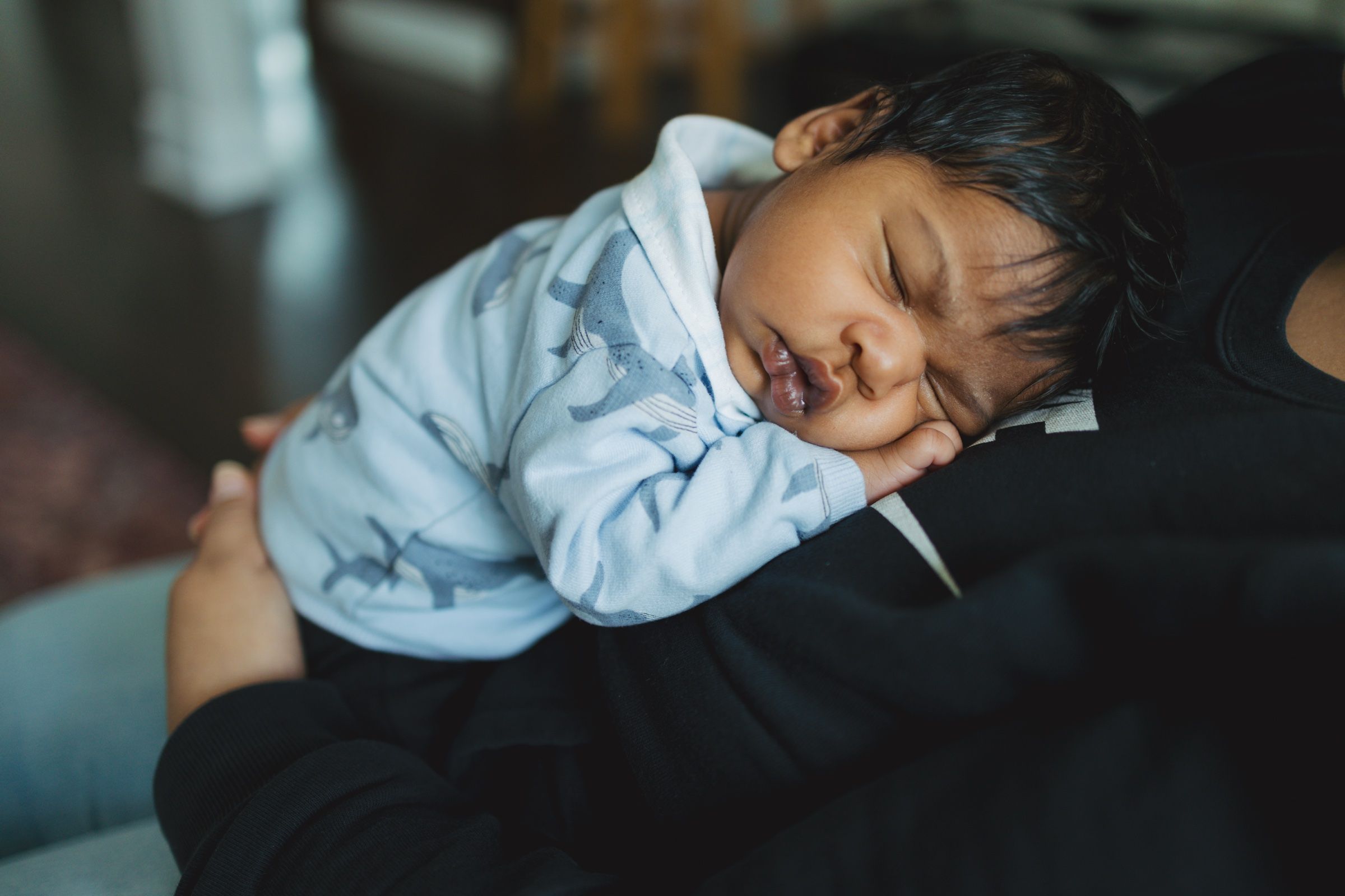 Sleeping baby boy in a whale-print onesie cradled in his mother's arm