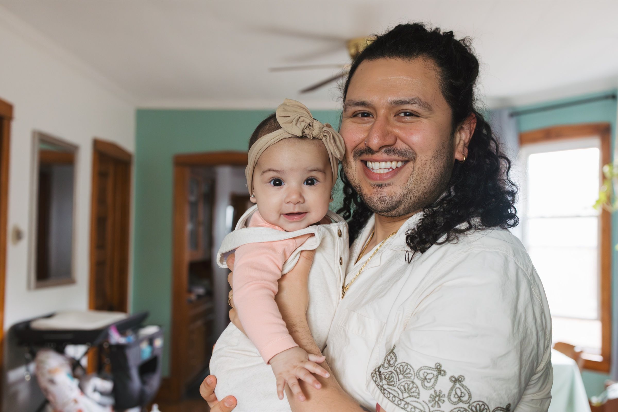 Father with long hair smiling while holding his infant daughter